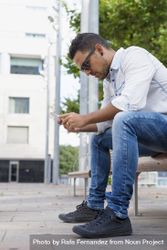 Side View Of Male Sitting On Bench Looking Down At Phone Free Photo