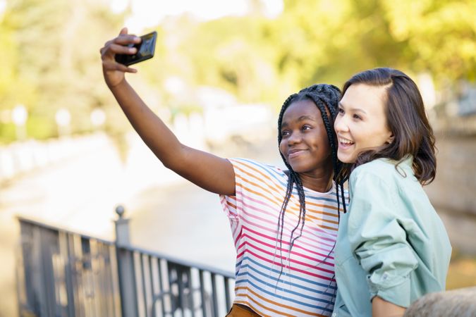 Women friends taking selfie with phone in casual clothing outside