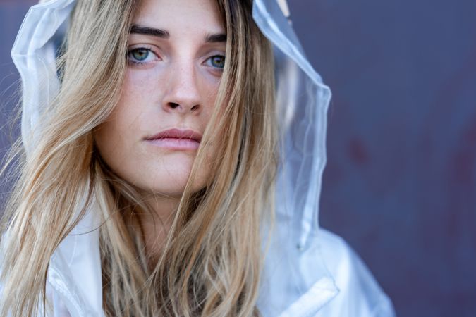 Charming stylish woman in raincoat sitting near wall