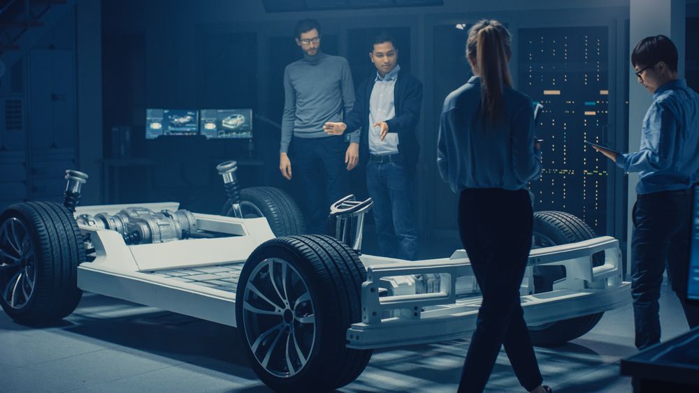 Team of Automotive Engineers Working on Electric Car Chassis Platform, Taking Measures, working with 3D CAD Software