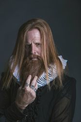 Confident adult red haired medieval magnate touching beard and looking at camera