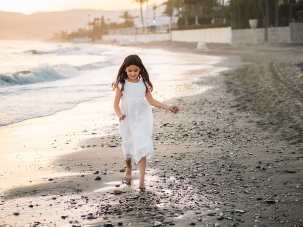 Adorable girl walking on seaside at sunset