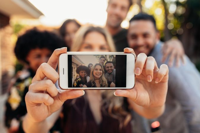 Woman taking self portrait with friends at outdoors party