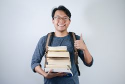 Asian young male student wearing bag and holding book smiling and happy expression