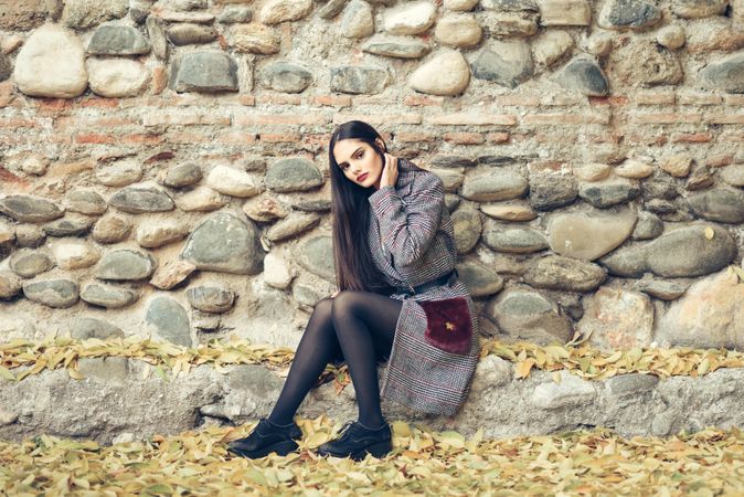 Female looking at camera adjusting hair in warm winter clothes sitting in front of rock wall