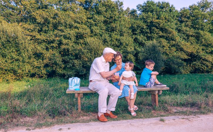 Older man feeding baby girl sitting in a bench