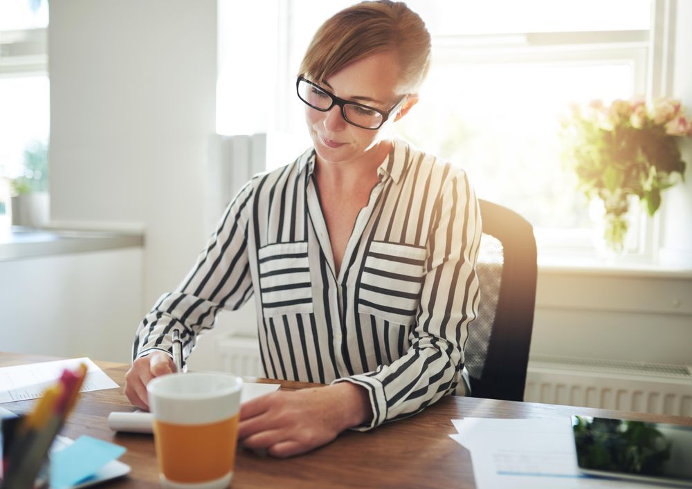 Woman in striped shirt taking notes at her bright home office