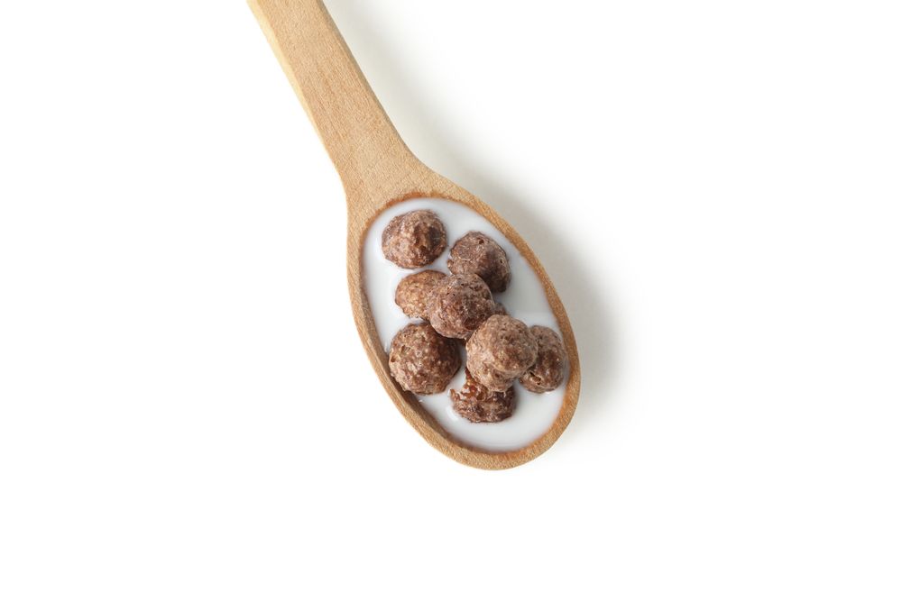 Spoon with corn balls and milk isolated on plain background