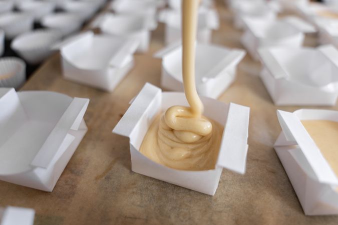 A baker woman is filling paper molds to prepare cupcakes. Close up