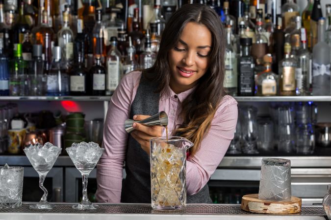 Smiling bartender pouring whiskey to a stirring glass
