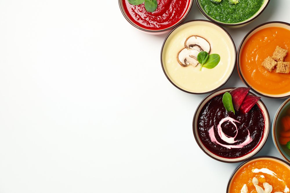 Multi-colored soups in corner of plain background with copy space