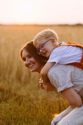Cheerful mom giving piggyback ride to cute son on wheat field