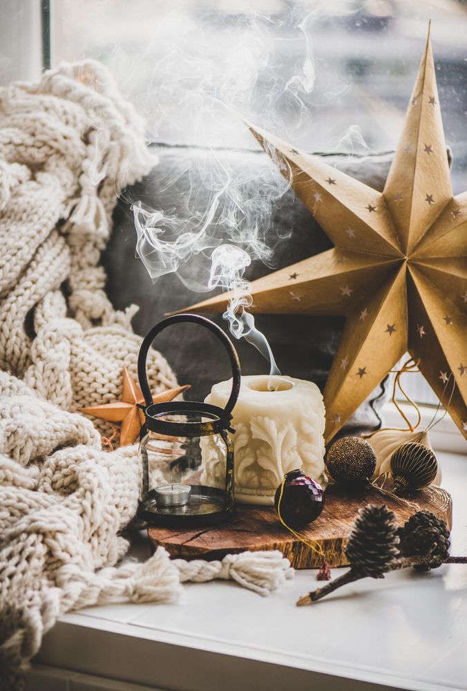 Extinguished candle, festive gold star and pine cone decorations with woolen blanket