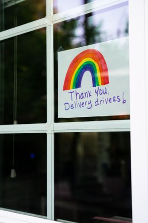 Handwritten sign with colored rainbow hanging in house window thanking delivery drivers