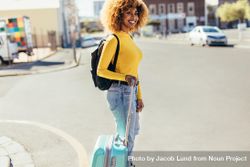 Smiling woman traveller standing on street with luggage waiting for a cab 4Z6ar4