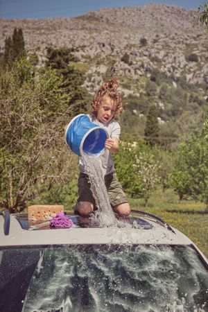 Cheerful boy washing car in countryside