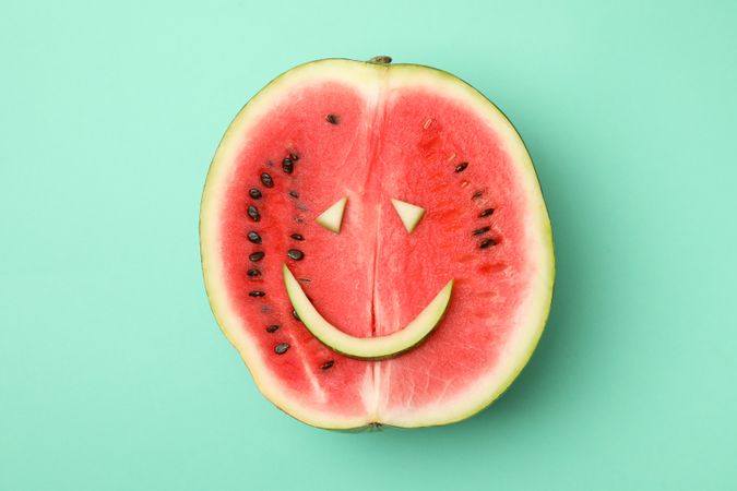 Watermelon with smiley face on mint background, top view