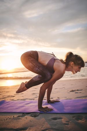 Woman doing yoga with sunset sky in background at beach