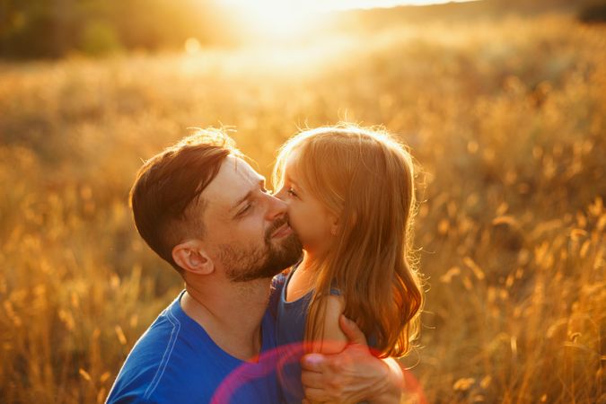 Female child hugs her father in field at dusk