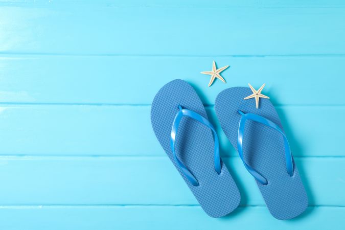 Flip flops and starfishes on color wooden background, space for text and top view. Summer vacation backdrop