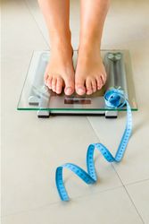 Woman feet standing on bathroom scale and tape measure