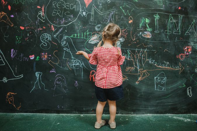 Girl drawing at school in writing green board