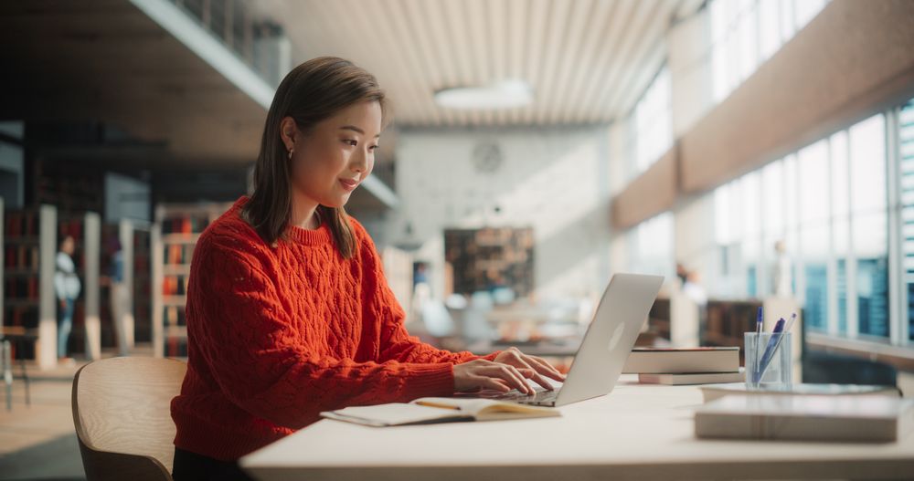 Diligent Asian Female Student Engaged in Online Learning at a Modern Library.