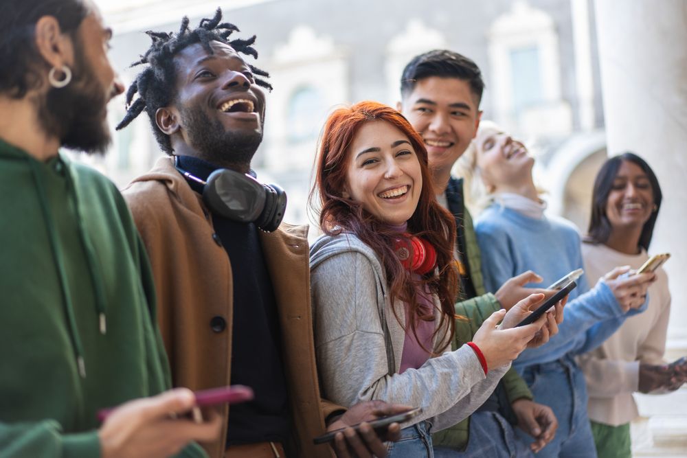 Laughing students standing around campus joking around and checking their phones