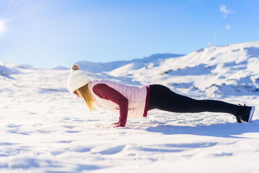 Side view of female in snowsuit doing pushup on snowy mountain