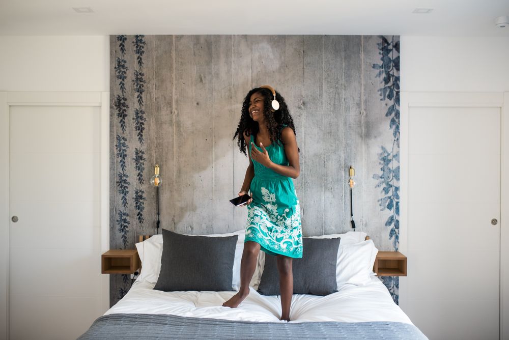 Black girl with headphones dancing on bed