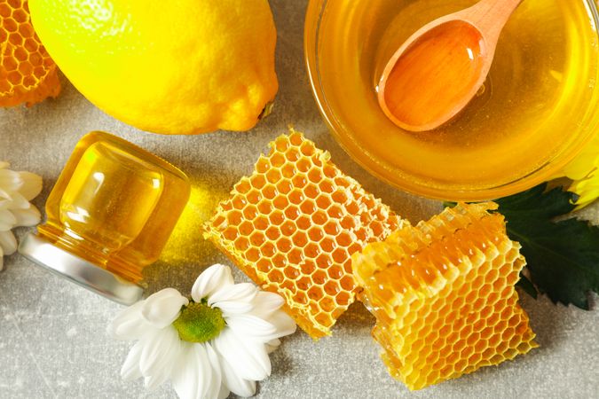 Honey, flowers and lemon on grey background, close up