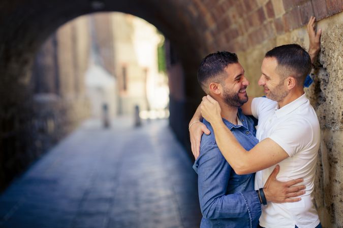 Two men facing each other in an embrace under a city bridge