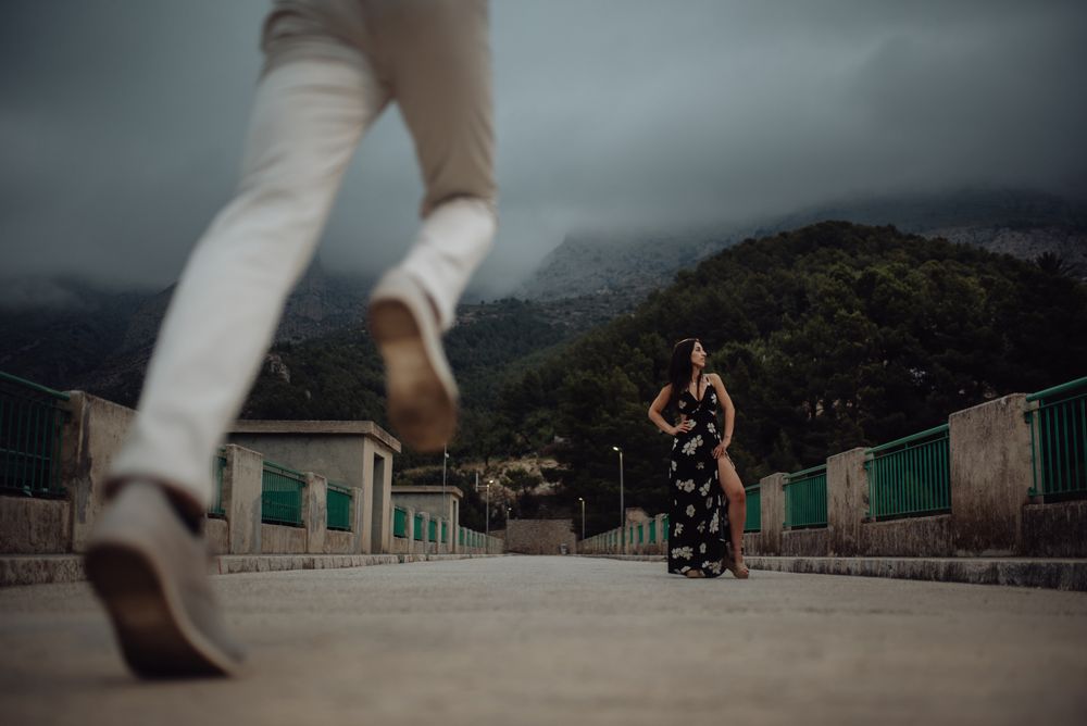 Man running to date with beautiful woman standing in long dress on stone bridge