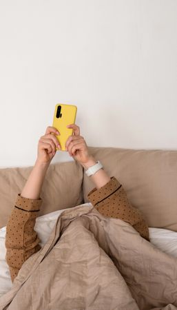 Hand with smartphone under covers