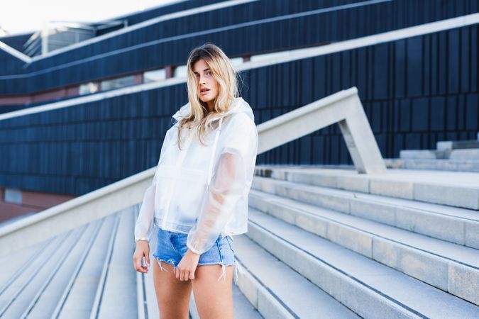 Charming stylish woman in raincoat standing on steps