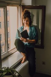 Interested woman reading book at window sill at home