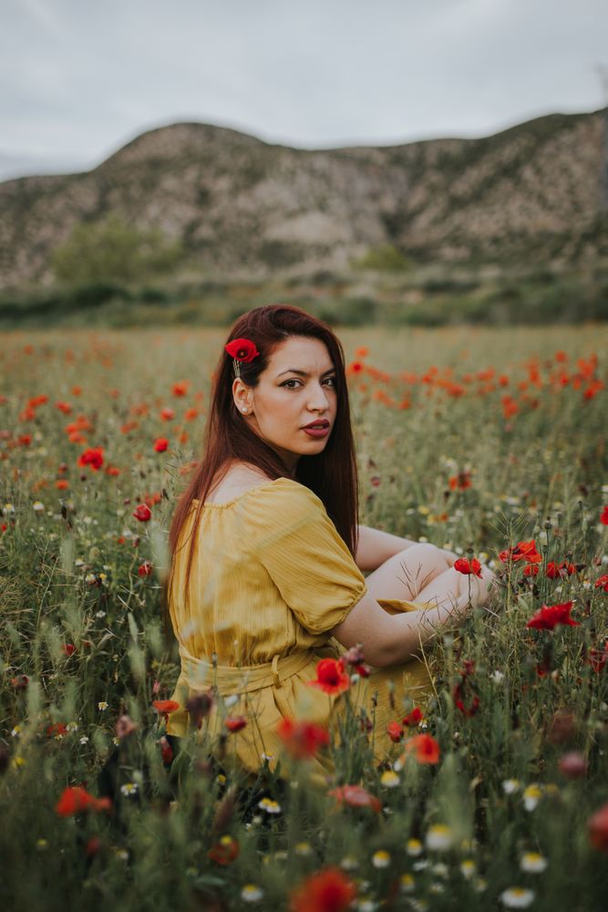 Woman sitting in field with poppies and daisies