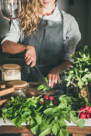 Blonde woman chopping fresh herbs with knife in rustic kitchen