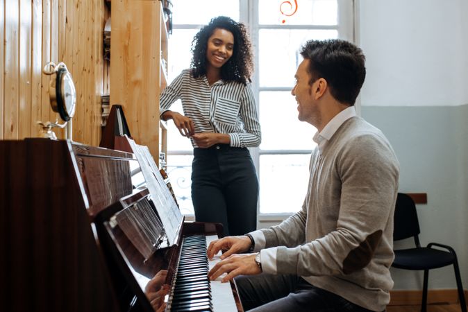 Man playing piano near woman teaching in studio