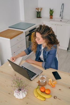 Female entrepreneur taking notes in notebook at home