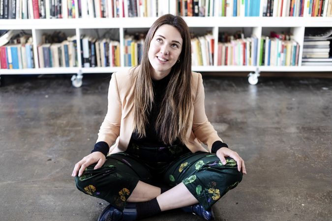 Portrait of a curious woman sitting cross legged in front of book shelf