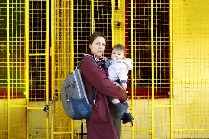 Side view of a woman standing with her child in front of yellow wall