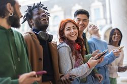 Laughing students standing around campus joking around and checking their phones