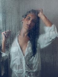 Thoughtful young woman standing behind misted glass with