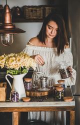 Woman in rustic kitchen putting loose tea leaves into tea pot