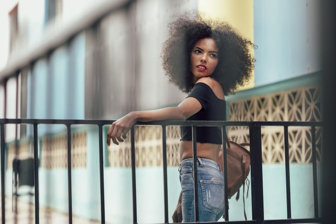 Young woman with afro hair standing near railings near a modern colorful building
