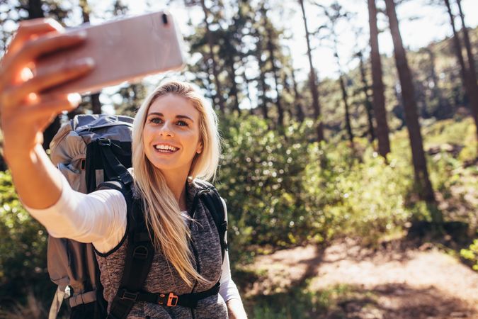 Blonde woman taking photograph using a mobile phone during trekking