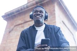 Smiling Black man outside, wearing headphones and holding phone 432lrx