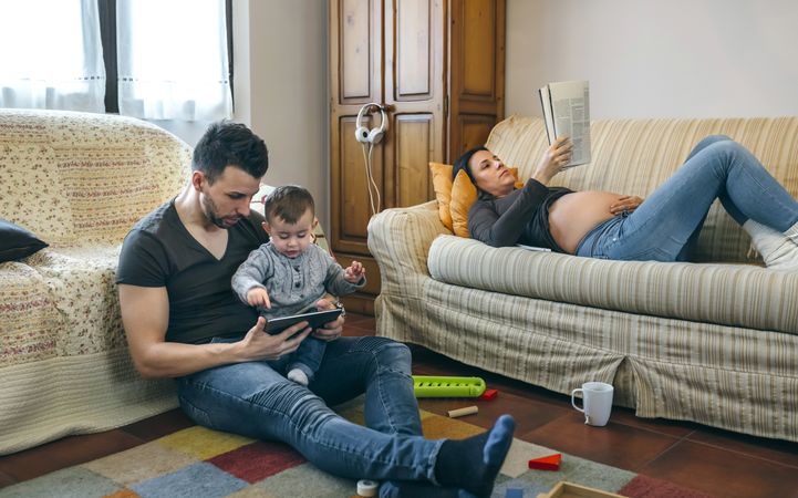 Father looking tablet with little son while the pregnant mother reads a magazine