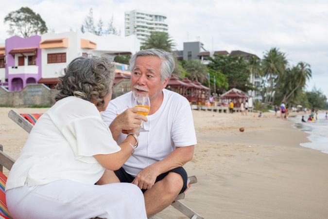 Older Asian couple relaxing on the beach with drinks